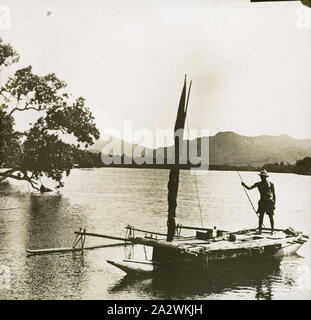 Diapositive - homme debout sur Outrigger Canoe, vers 1930, diapositive sur Noir et blanc avec une photographie de l'homme tenant une lance sur un poteau ou une pirogue, montagnes au loin vers 1930 Banque D'Images