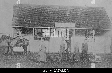 Négatif - Horse Rider & groupe familial d'une Shingle-Roofed Building, l'Australie, vers 1895, un groupe devant un magasin ou à l'hôtel, qui dispose d'un toit en ardoise et d'une cheminée. Il y a un homme à cheval sur la gauche et il y a un cheval à bascule à côté des enfants sur la droite. L'homme sur le cheval porte un chapeau, et la femme porte une robe Banque D'Images