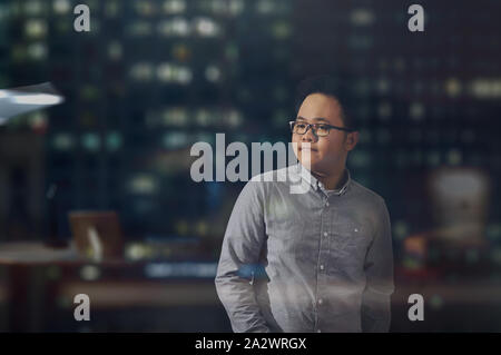 Young businessman wearing dans une pose assurée et heureux à l'intérieur d'un immeuble de bureaux dans la nuit. Homme debout et en regardant son côté gauche en observation. Banque D'Images