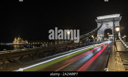 Pont à chaînes Széchenyi éclairé la nuit à Budapest avec le Parlement en arrière-plan et lisse, feux rouge trace la Hongrie Banque D'Images