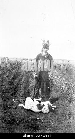 Négatif - District de Mildura, Victoria, vers 1920, un homme portant un costume indien. C'est prêté par Rhodes motor bikes à porter comme une promotion publicitaire pour les motos. Il est dans un vignoble et a deux chiens à ses pieds Banque D'Images