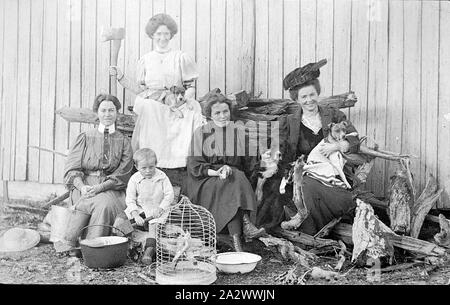 Point négatif - Pique-nique, Victoria, vers 1915, quatre femmes et un petit garçon assis sur une pile de journaux. Deux femmes occupent des chiens, l'un détient également une hache. Le petit garçon est titulaire d'un jouet chat et une autre femme un seau. Il y a un cacatoès dans une cage devant le groupe Banque D'Images