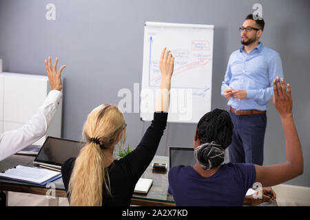 Groupe d'employés lèvent la main au cours de la présentation dans la salle de réunion Banque D'Images