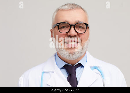 Portrait of mature médecin avec les cheveux gris et sa barbe wearing eyeglasses smiling at camera sur fond blanc Banque D'Images