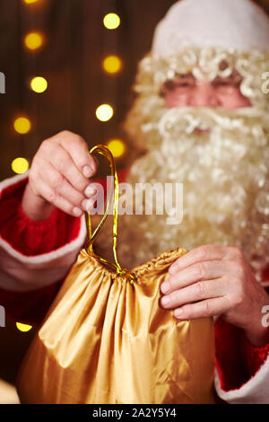 Le Père Noël ouvre un sac de cadeaux, assis près de l'arbre de Noël décoré avec des lumières - Joyeux Noël et bonnes fêtes ! Banque D'Images