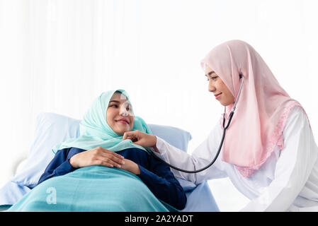 Une belle jeune médecin musulman est à l'aide d'un stéthoscope pour écouter le rythme cardiaque du patient au lit dans l'hôpital salle d'examen. Banque D'Images