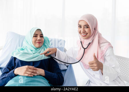 Une belle jeune médecin musulman est à l'aide d'un stéthoscope pour écouter le rythme cardiaque du patient au lit dans l'hôpital salle d'examen. Banque D'Images