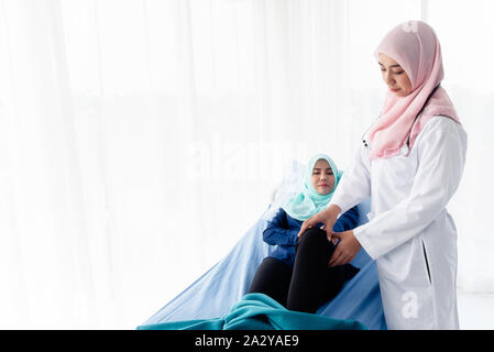 Une belle jeune femme musulmane portant un stéthoscope est médecin examinant les genoux du patient allongé sur le lit dans la salle d'examen à l'hos Banque D'Images