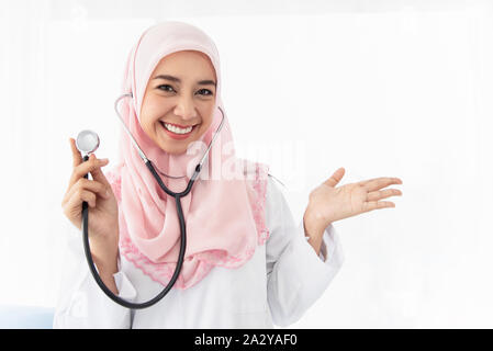 Portrait d'une belle jeune femme médecin musulmane montre sa main gauche et portant un stéthoscope et sourires permanent dans une salle d'examen à l'hosp Banque D'Images