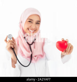 Portrait de la belle jeune femme musulmane médecin montre un cœur rouge sur la main gauche et portant un stéthoscope et sourires permanent dans un examen roo Banque D'Images