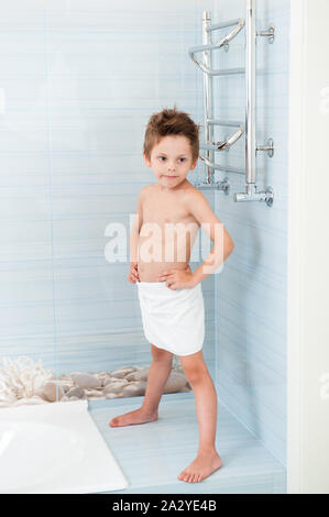 Petit mignon sain boy wearing serviette blanche debout dans une salle de bain propre bleu Banque D'Images