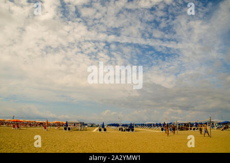 Vue panoramique sur la plage de sable avec des rangées de parasols et les jeunes à jouer au volleyball de plage dans une journée ensoleillée, Viareggio, Toscane, Italie Banque D'Images