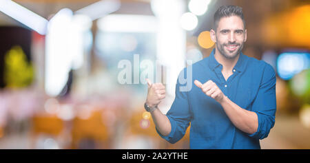 Jeune homme séduisant sur fond isolé en pointant sur l'arrière derrière avec la main et Thumbs up, souriant confiant Banque D'Images