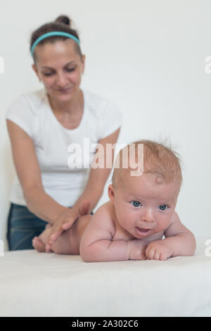 Une femme en dehors de la vue de faire des massages à un jeune enfant. Funny baby au premier plan ramper en avant sur la table Banque D'Images