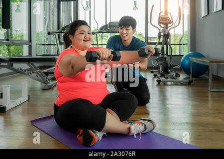 Deux formateurs de l'Asie et de l'embonpoint homme woman exercising with dumbbell ensemble dans une salle de sport moderne, heureux et sourire pendant l'entraînement. Grosses femmes prendre soin de hea Banque D'Images