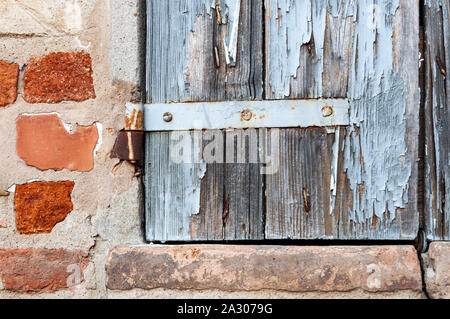 Détail de la fenêtre de maison rurale, avec peinture craquelée et charnières rouillées, sur mur de briques et de pierres anciennes. Banque D'Images