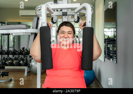 Surpoids asiatique femme jouant de l'équipement de sport pour l'exercice de bâtir sa boday seul dans une salle de sport, plaisir et sourire pendant l'entraînement. Grosses femmes prendre soin de la santé Banque D'Images