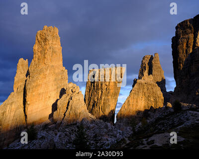 Formation de roche grisâtre pâle de Cinque Torri tournant en rouge sur un fond de nuages sombres au coucher du soleil. Cortina d'Ampezzo, Dolomites, Vénétie, Italie. Banque D'Images