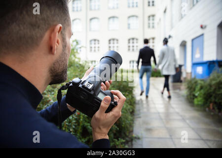 Jeune homme Photographe Paparazzi Capture d'une photo de couple étrangement marcher ensemble à l'aide d'une caméra Banque D'Images