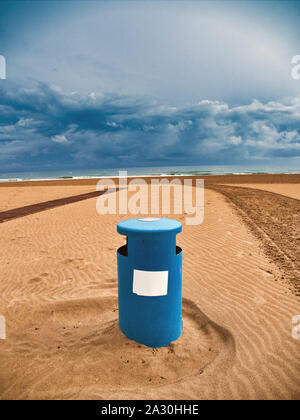 Close-up d'une poubelle bleue sur la plage de Gandia, Valence, sur une journée avec le ciel couvert de nuages et de pluies Banque D'Images