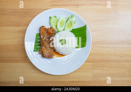 Côtes de porc et du riz sur des feuilles de bananier avec concombres sur une plaque blanche sur table en bois. Banque D'Images