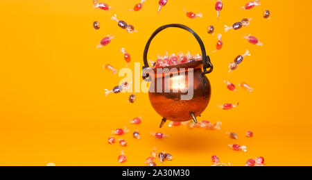 Pot de fer avec des caramels multicolores sur fond orange vide. Halloween de concept Banque D'Images