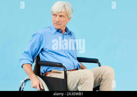 La haute mobilité man in blue shirt assis en fauteuil roulant contre le fond bleu Banque D'Images