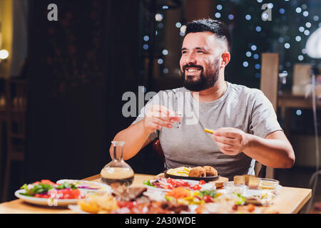 Homme boit de la vodka sur une grande table avec des aliments gras et des collations Banque D'Images