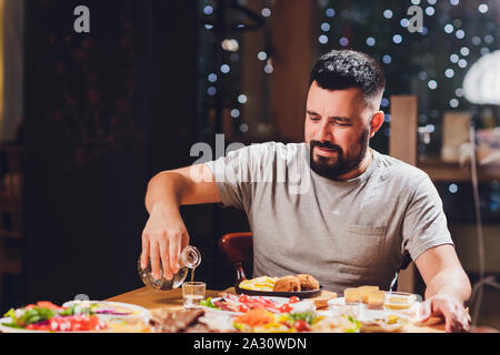 Homme boit de la vodka sur une grande table avec de la nourriture et des collations Banque D'Images