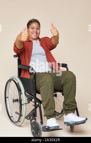 Portrait of African professionnels mobilité femme assise en fauteuil roulant et showing Thumbs up pour l'appareil photo contre le fond blanc Banque D'Images