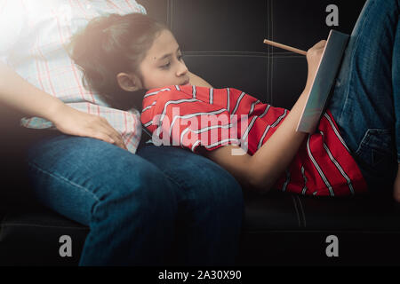 Fille portant sur sa mère et de faire leurs devoirs à la maison sous la lumière chaude. Concept de l'éducation. Banque D'Images