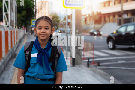 Lycéenne en uniforme de la jeunesse Croix-Rouge thaïlandaise avec sac à dos sur le trottoir sous la lumière du soleil. Banque D'Images