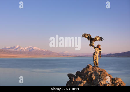 Kazakh traditionnel eagle hunter avec son aigle doré en face d'une montagne à une rive du lac. Ulgii, l'ouest de la Mongolie. Banque D'Images