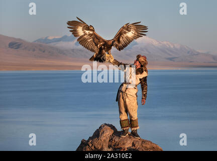 Kazakh traditionnel eagle hunter avec son aigle doré en face d'une montagne à une rive du lac. Ulgii, l'ouest de la Mongolie. Banque D'Images