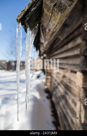 Les glaçons pendent du toit d'une vieille cabane sur un beau jour de printemps, dans le village. Banque D'Images