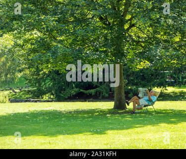 Homme assis dans un transat, lire un journal sur la journée la plus chaude de l'année 2019 dans la région de pavilion gardens dans le peak district ville de Buxton Banque D'Images