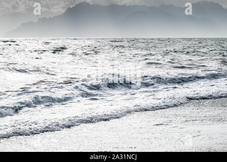 Les vagues de la mer blanche laiteuse et rive avec balle unique sur l'eau et la montagne d'ossature Banque D'Images