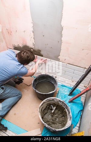 Mâle - professionnel met les carreaux dans la salle de bains privative avec une solution qui est stocké dans le godet et l'outil. Banque D'Images