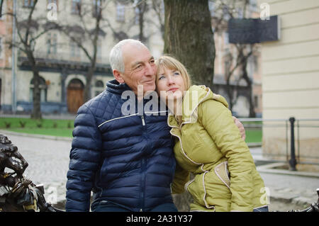 Bel homme âgé est embrassant sa jeune femme blonde de passer du temps ensemble à l'extérieur dans l'ancienne cité au début du printemps ou en automne. Banque D'Images