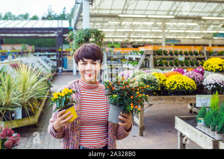 Young caucasian woman holding des pots avec des plantes ornementales et de cerisier d'hiver les poivrons dans un centre de jardinage. L'automne et l'hiver des idées pour décorer. Un passe-temps Banque D'Images