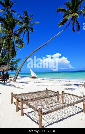 La plage tropicale à Zanzibar - eaux claires, lit de bronzage et le palmier. Ciel bleu clair. Banque D'Images