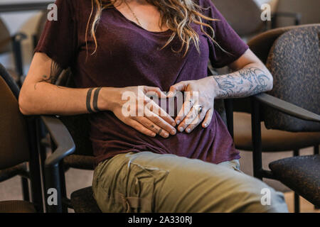 Une vue en gros plan sur le bras tatoué d'une femme enceinte en appui sur les mains de bébé, échographie bump hôpital salle d'attente. Banque D'Images