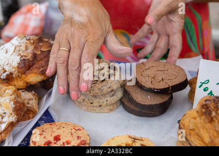 Mains d'un baker sont vus close-up, l'organisation de biscuits fraîchement cuits au four sur un stand lors d'un marché d'agriculteurs de vendre des aliments produits localement. Banque D'Images