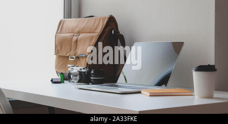 Espace de travail confortable avec un ordinateur portable ouvert avec sac postal et des fournitures de bureau en regard de windows Banque D'Images