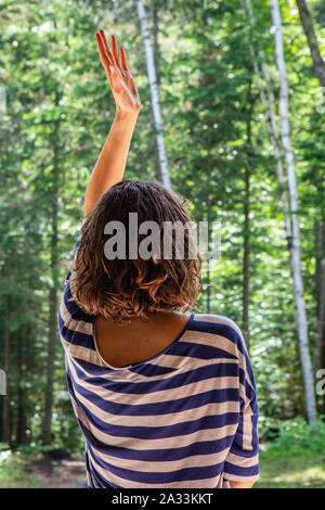 Une jeune dame dynamique libre est vu de derrière avec un bras soulevé dans l'air lors d'une série d'exercices chamaniques dans un environnement naturel à multicultural retreat Banque D'Images