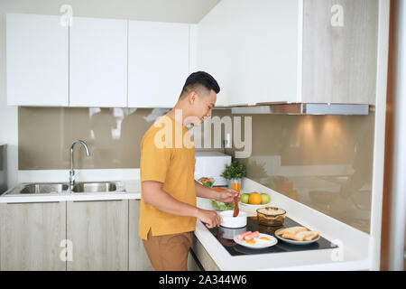 Heureux l'homme asiatique préparer la nourriture dans la cuisine à la maison. Banque D'Images