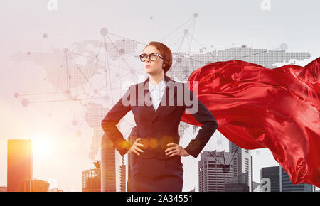 Young confident businesswoman wearing red cape contre l'arrière-plan la ville moderne Banque D'Images