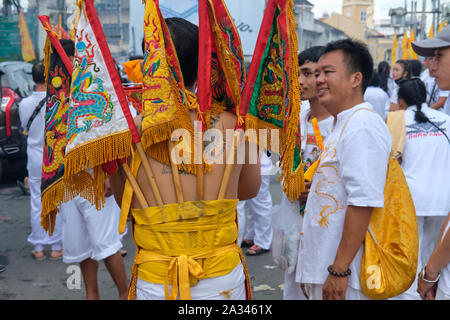 Une procession pendant le Festival végétarien dans la ville de Phuket, Thaïlande avec un participant affichant des drapeaux sacrés attachés à son dos Banque D'Images