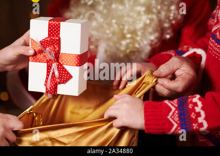Le Père Noël ouvre un sac et donne des cadeaux aux enfants, assis près de l'arbre de Noël décoré avec des lumières - Joyeux Noël et bonnes fêtes ! Banque D'Images