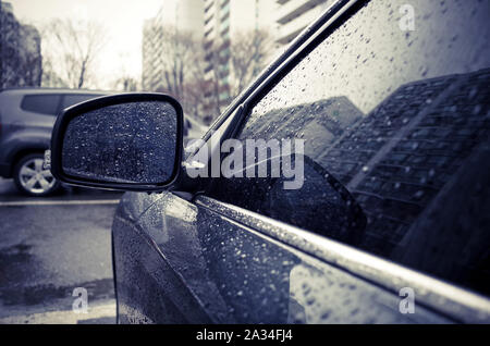 Gouttes de pluie sur rétroviseur latéral en jour de pluie. Banque D'Images